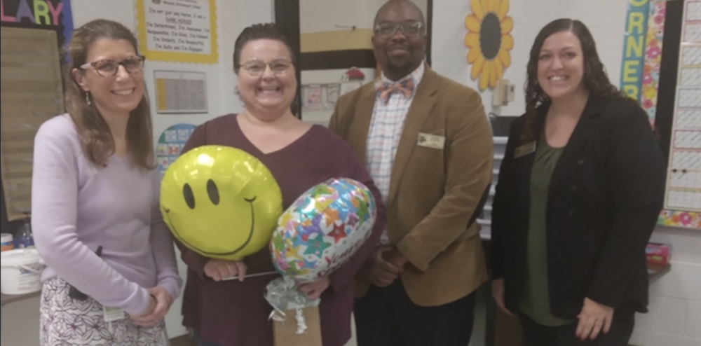 4 people smiling for a picture while holding balloons